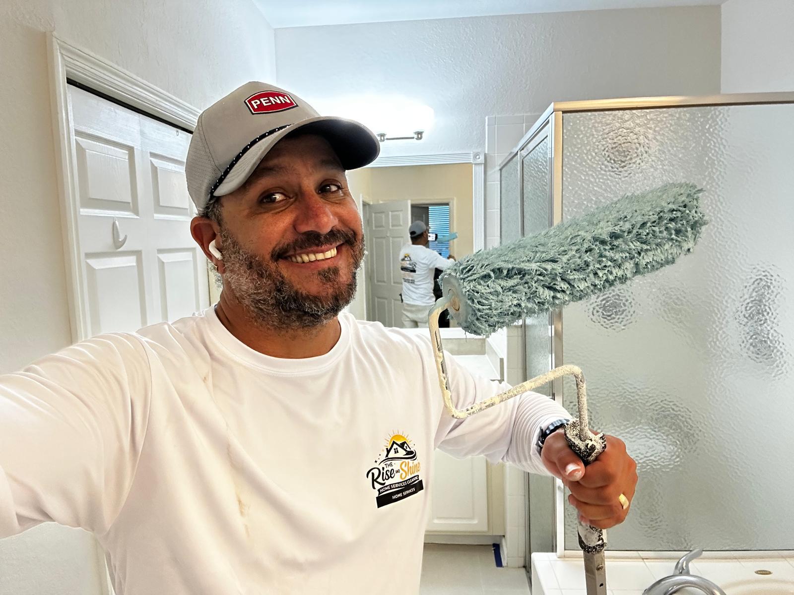 Rise and Shine painter smiling with a paint roller in a bathroom